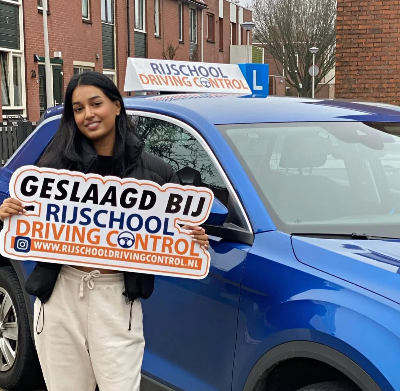 Geslaagd bij Rijschool Driving Control — leerling met Geslaagd-bord naast blauwe lesauto met daklogo in Rotterdam