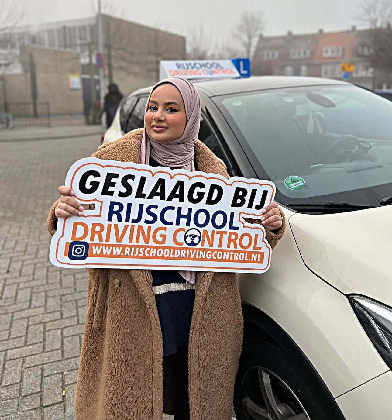 Geslaagde vrouwelijke autoleerling met Geslaagd-bord Rijschool Driving Control bij witte lesauto in Rotterdam